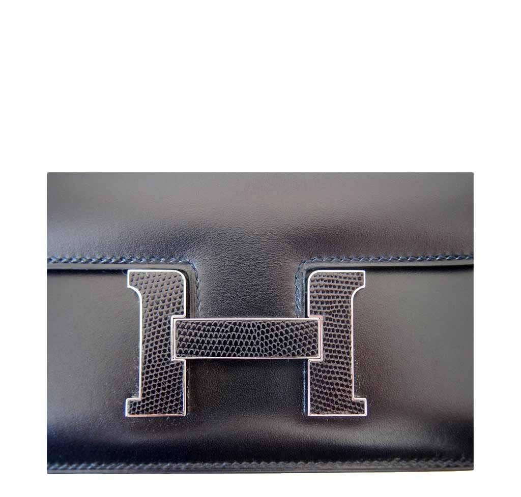 Black leather clutch with silver 'H' logo on a white background