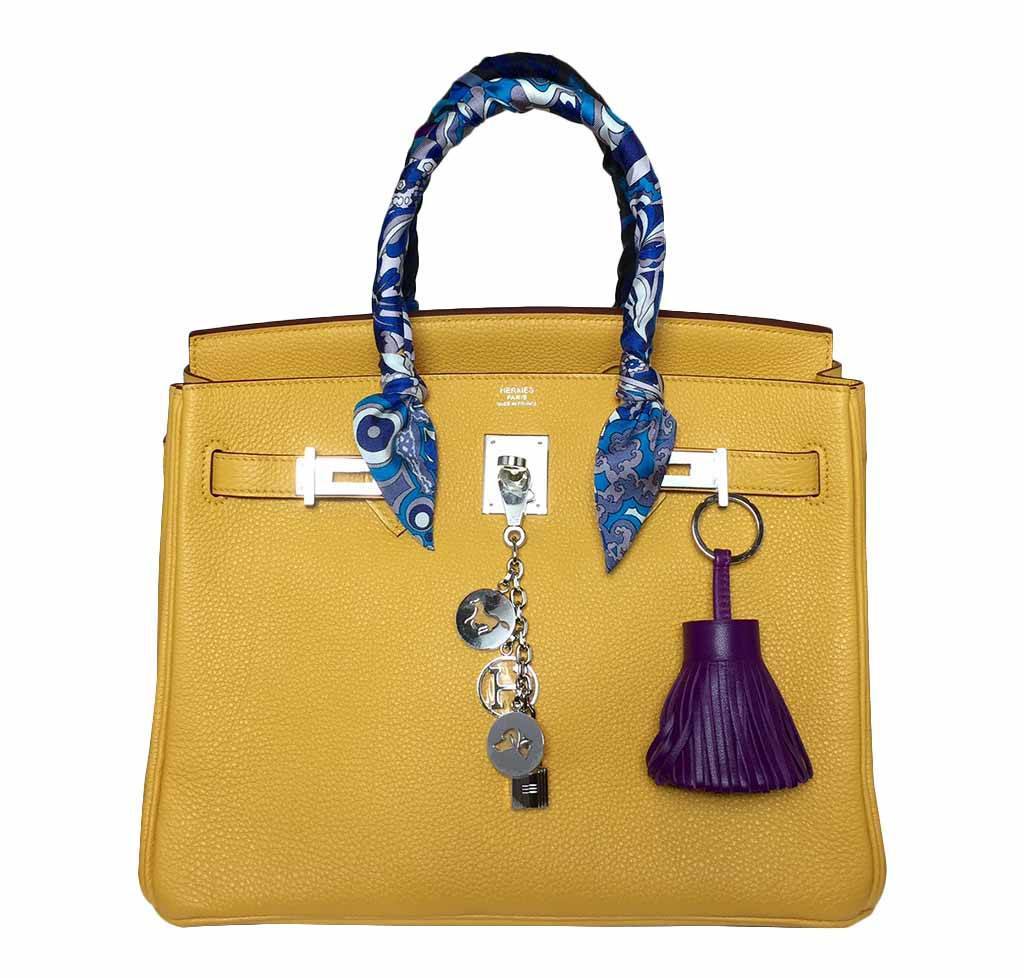 Yellow handbag with blue floral handle and various charms on a white background