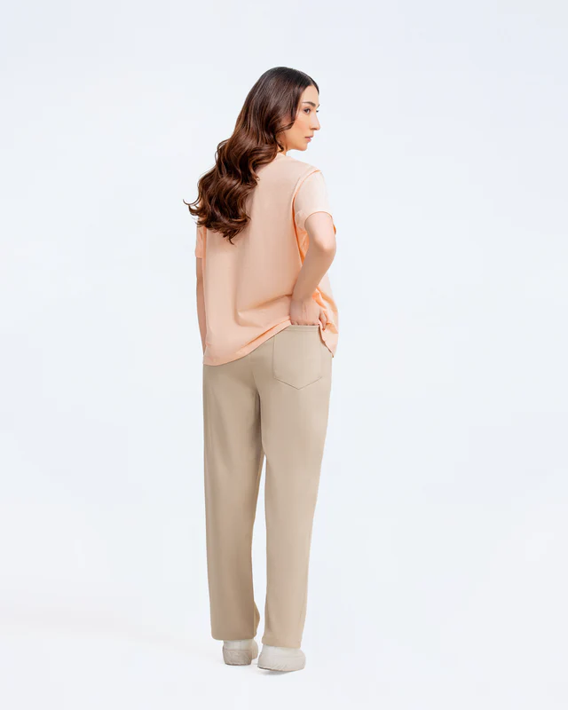 Woman wearing a peach top and beige pants on a white background