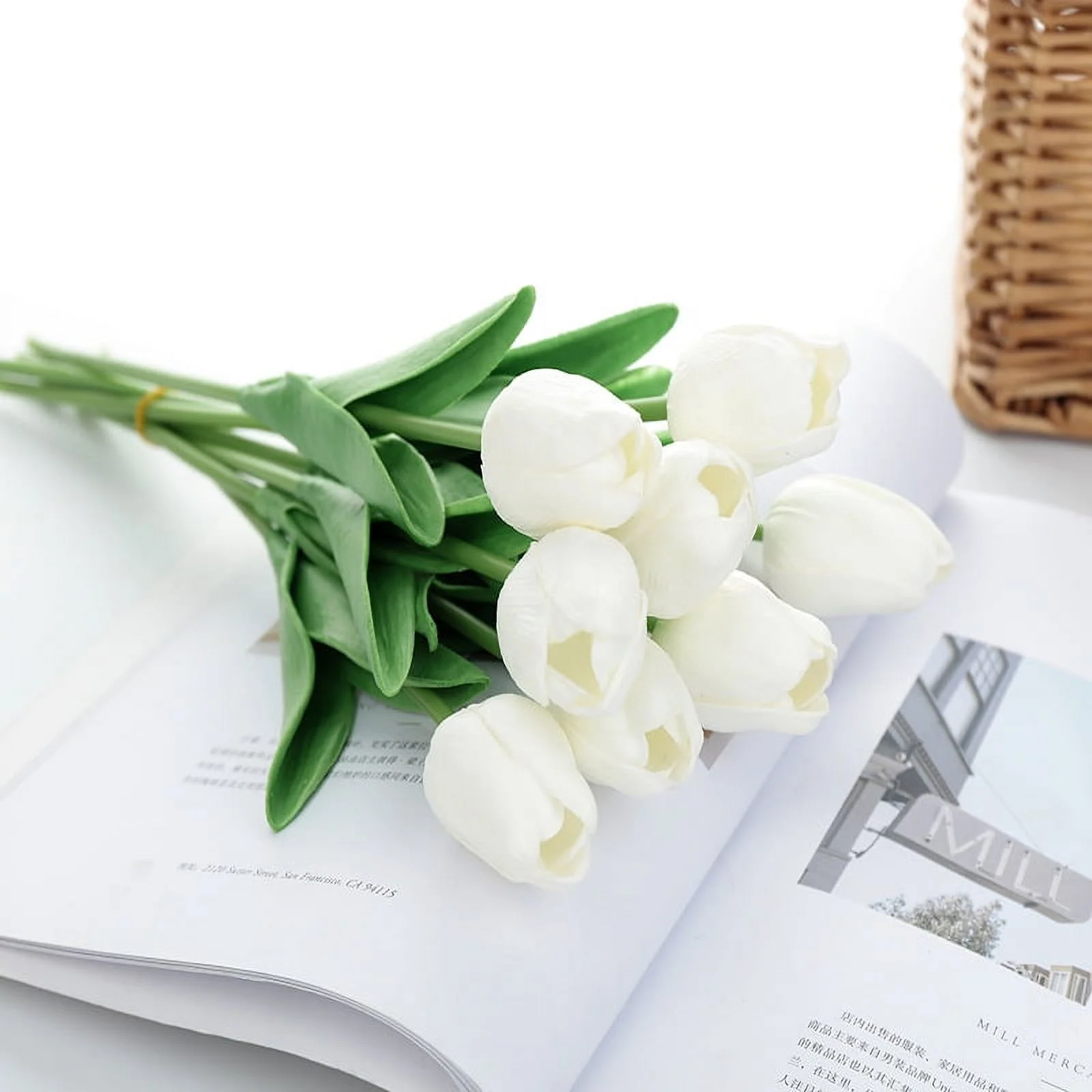 White tulips on an open magazine with a wicker basket in the background