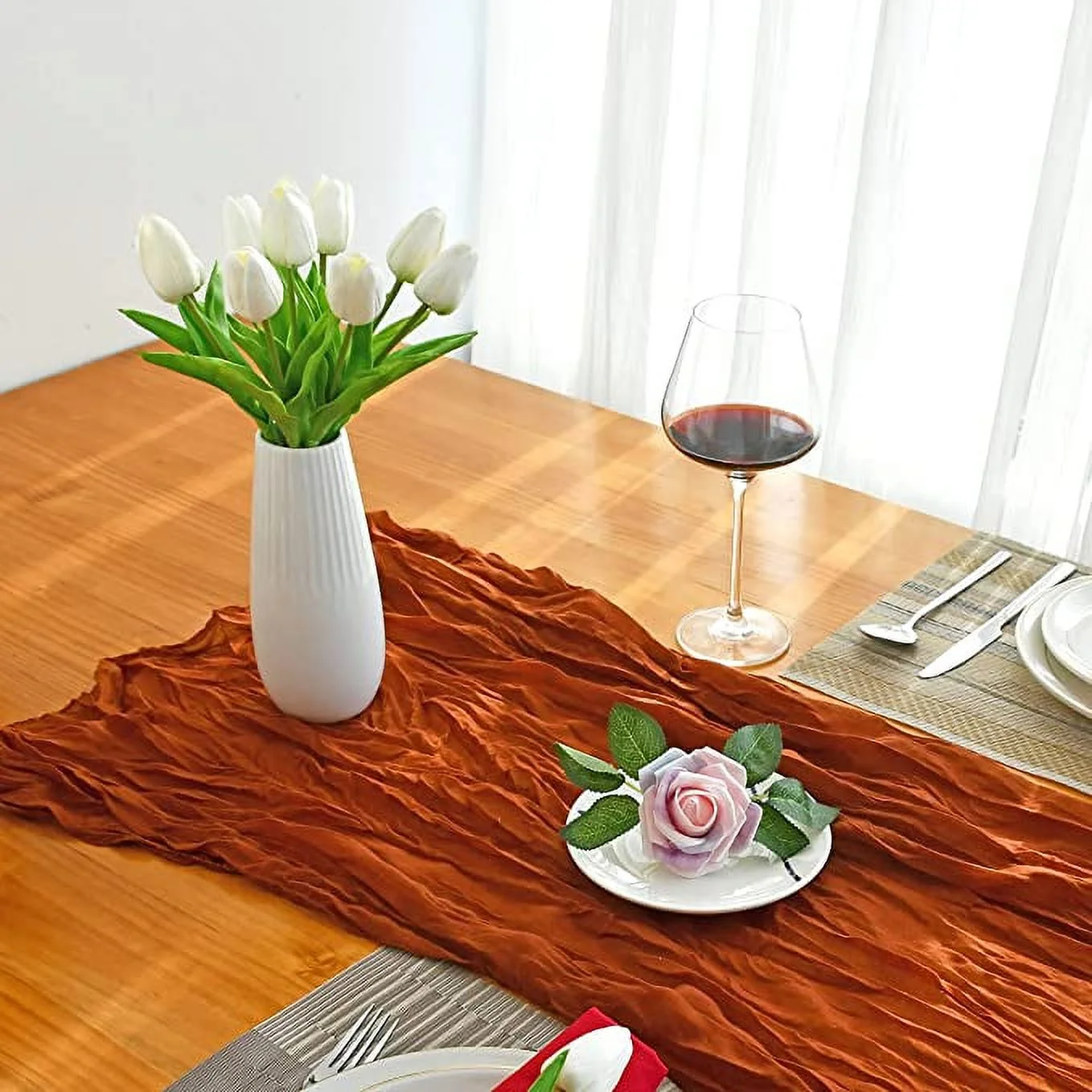 Decorative table setting with a vase of white tulips, a glass of red wine, and a small pink flower on a wooden table.