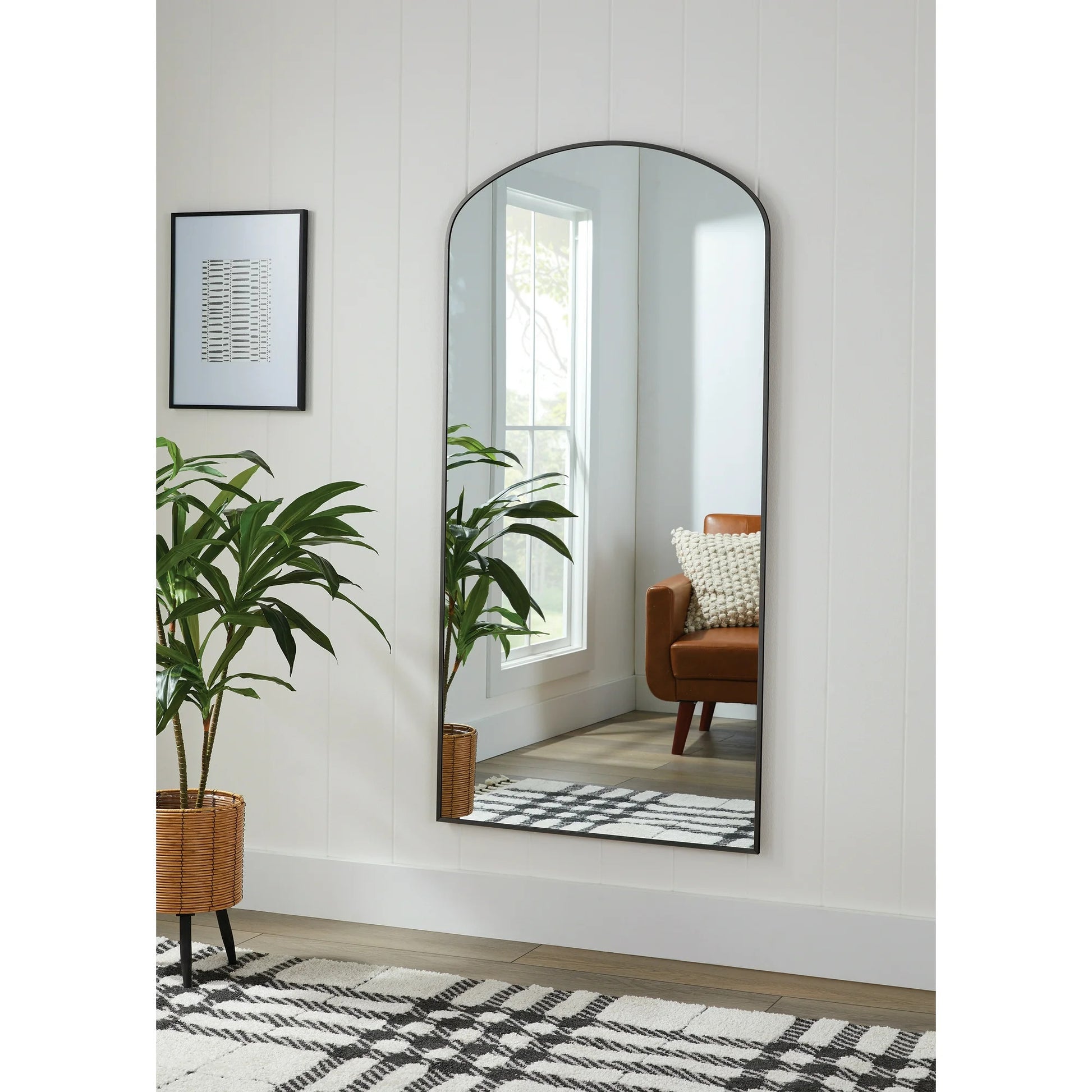Long, arched floor mirror in a room with a plant and a chair.