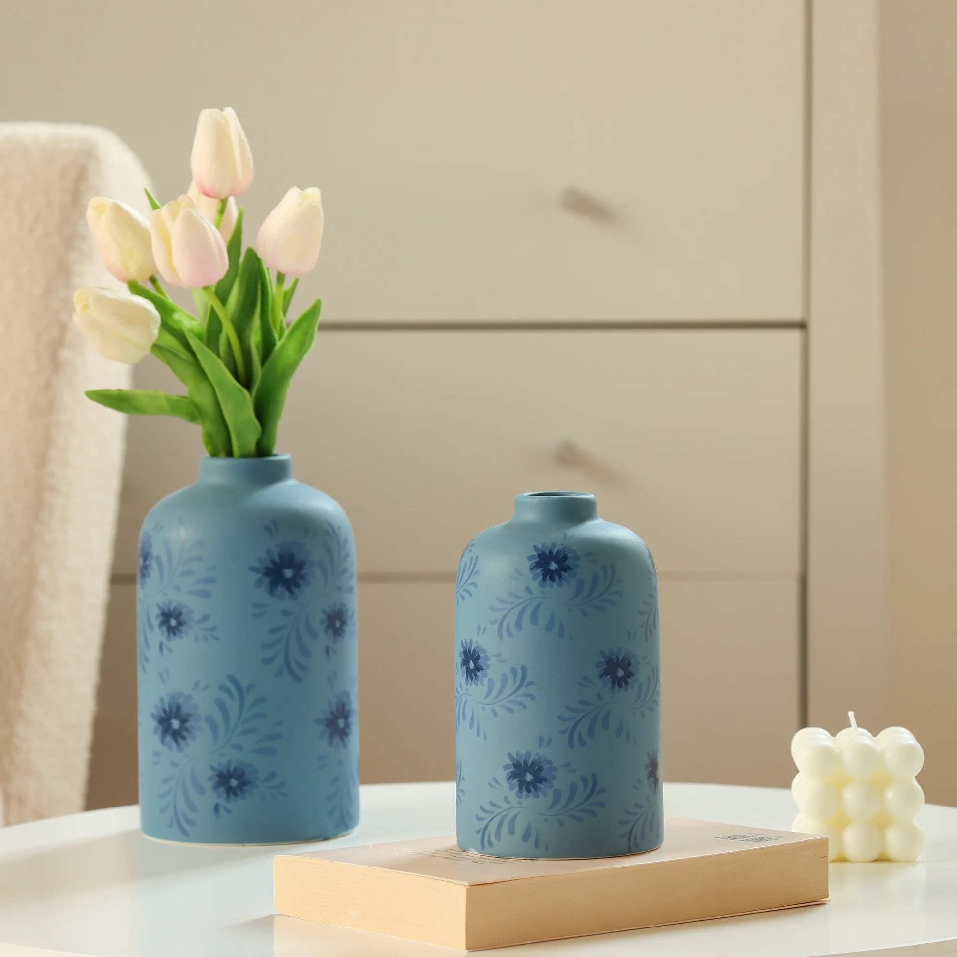 Two blue vases with floral patterns on a table with tulips and a candle.