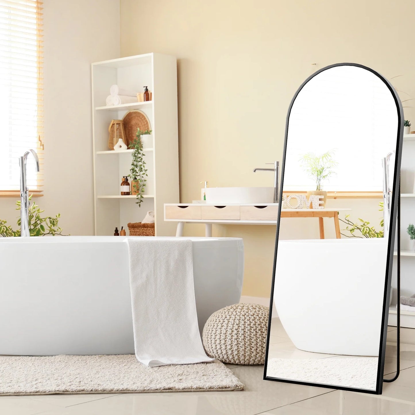 Full-length mirror in a bathroom setting with a bathtub and shelves.