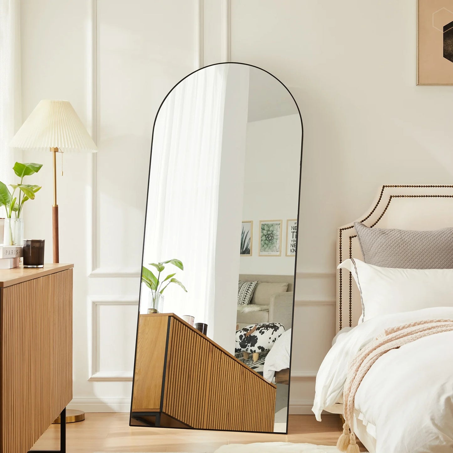 Large floor mirror in a bedroom setting with a bed and lamp.