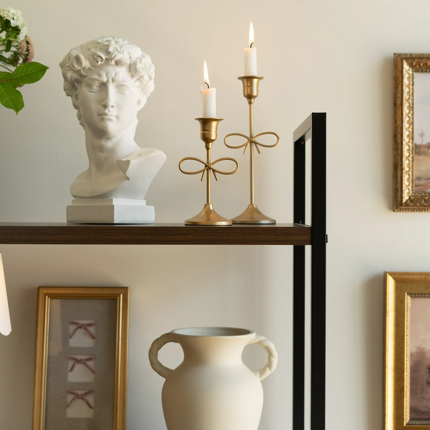 Decorative shelf with bust, candles, and vase against a neutral wall.