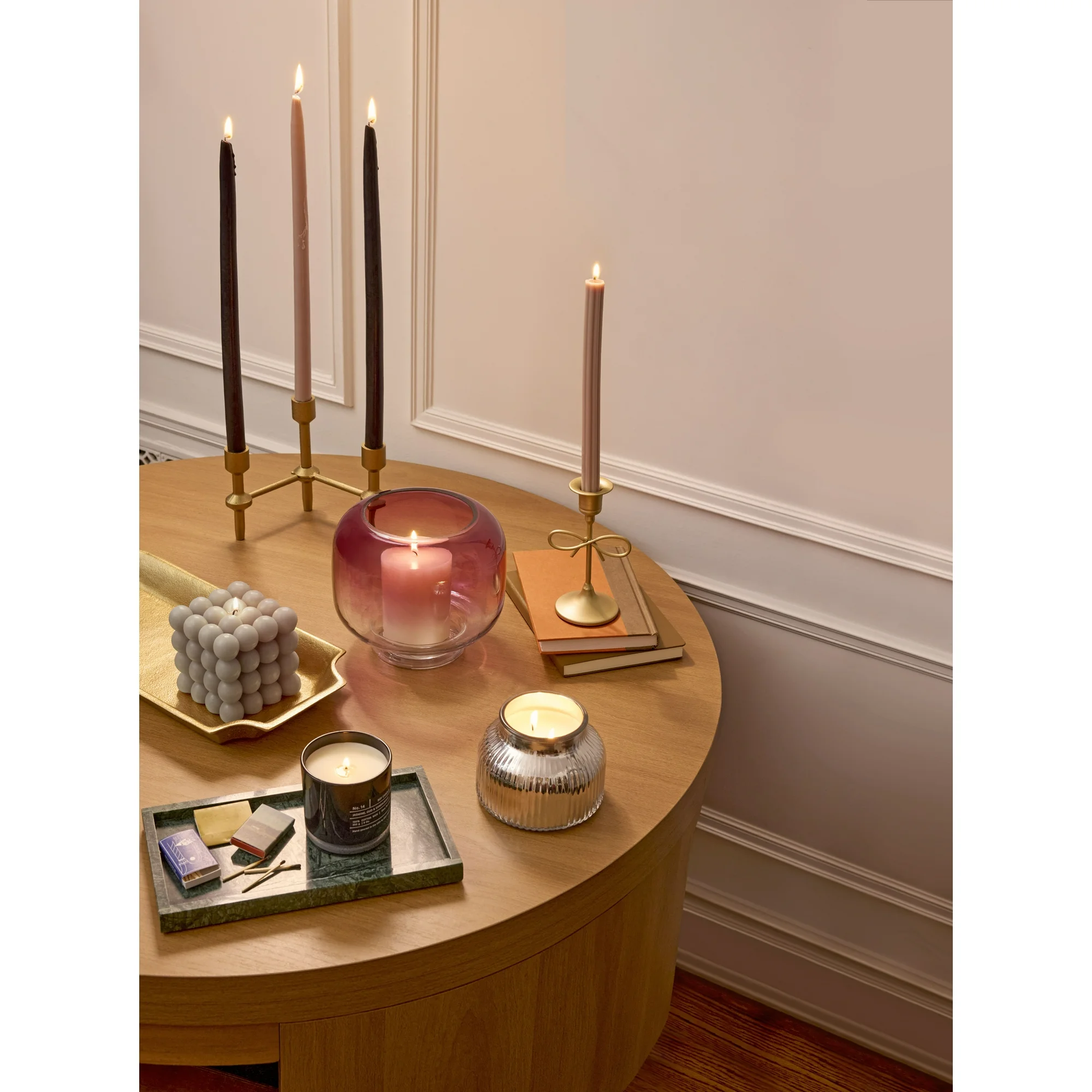 Round wooden table with decorative candles and items against a neutral wall.