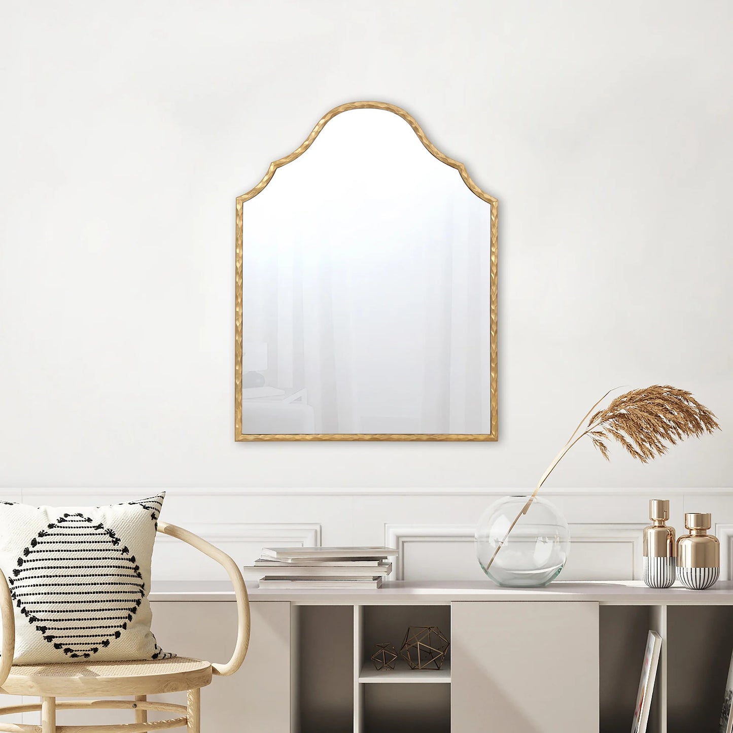 Decorative mirror with gold frame on a white wall above a shelf with decorative items.
