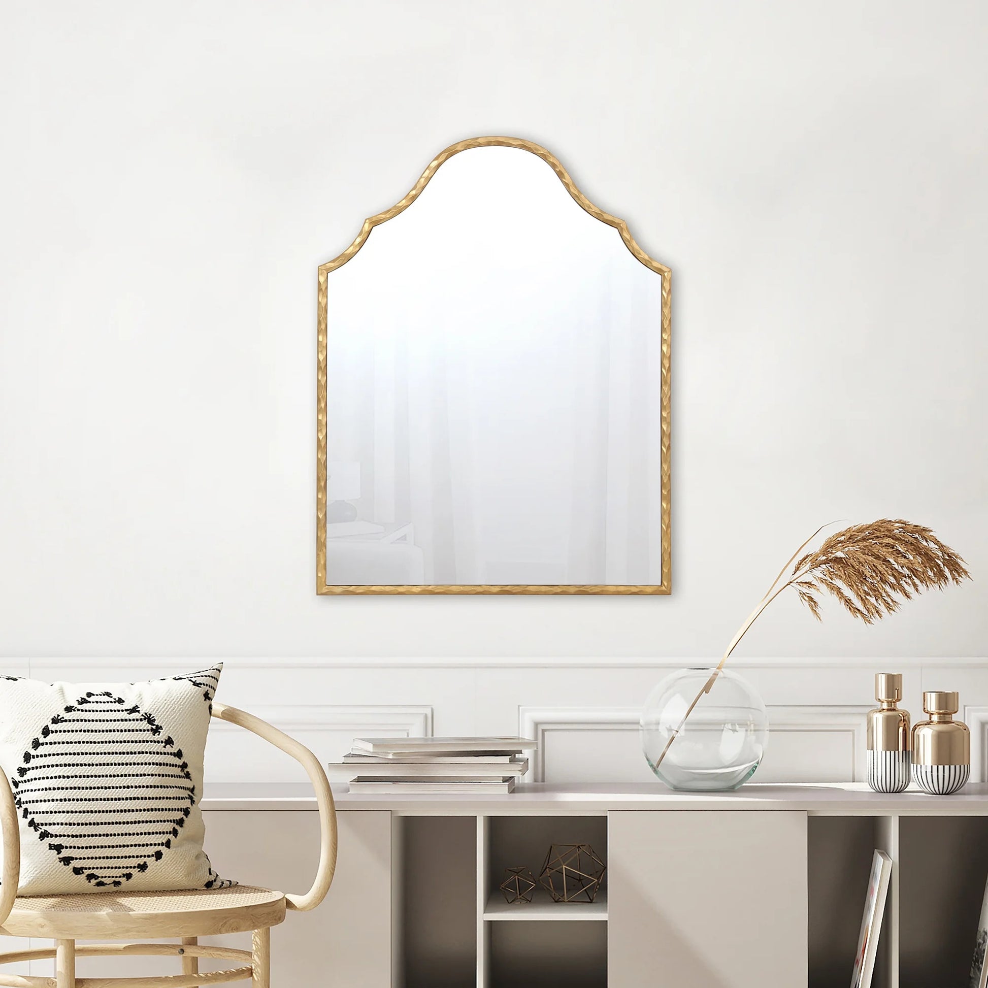 Decorative mirror with gold frame on a white wall above a shelf with decorative items.