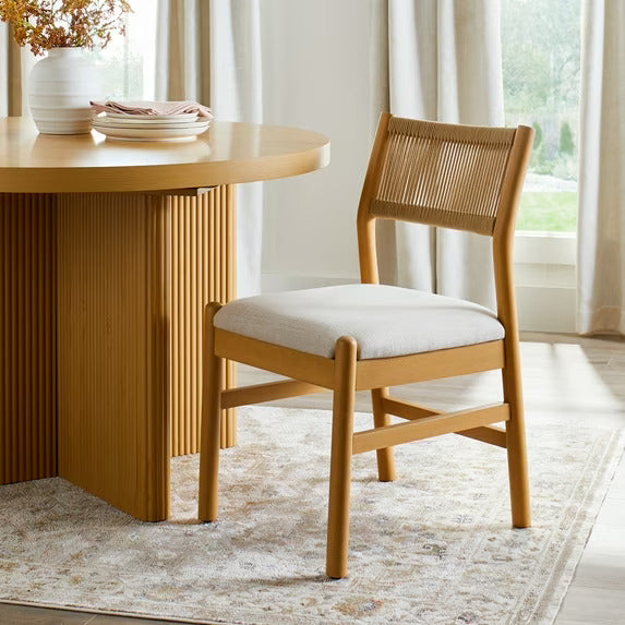 Wooden dining table with a chair in a bright room with curtains.