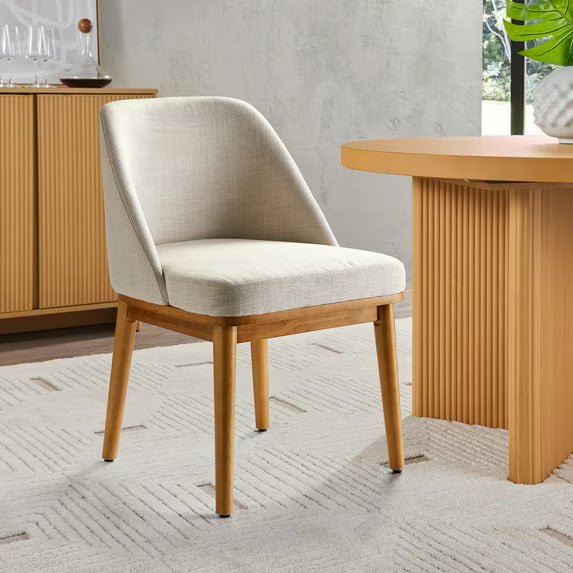 Beige chair with wooden legs in a room with a wooden table and cabinet.